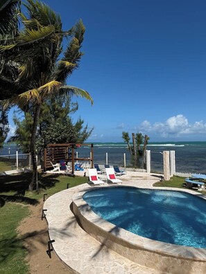 A pool area with lounge chairs, a wooden pergola, and a view of the ocean. - Beachfront, Spacious Home, Private Luxury Pool! (Palmer)