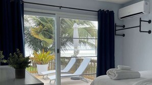A bedroom with a bed, a ceiling fan, a sliding glass door leading to a balcony with a pool, lounge chairs, and a potted plant. - Beachfront, Spacious Home, Private Luxury Pool! (Palmer)