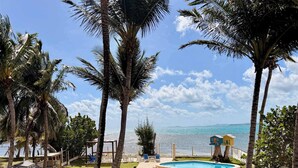 A pool area with a view of the sea, surrounded by palm trees and a wooden deck. - Beachfront, Spacious Home, Private Luxury Pool! (Palmer)