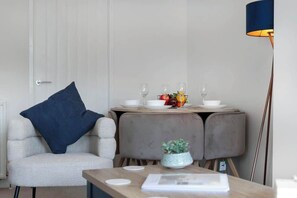 Ein modernes Zimmer mit einem weißen Stuhl, einem Tisch mit blauer Sitzkissen, einer kleinen Pflanze und einer Lampe.