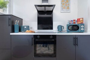 Eine Küche mit einem schwarzen Backofen, einer Mikrowelle und einem Toaster. Auf der Fensterbank steht ein Blumentopf.