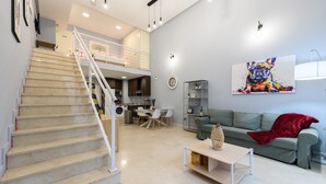 Un vaste espace de vie comprenant un escalier, une table à manger avec des chaises, un canapé et un tableau coloré accroché au mur.