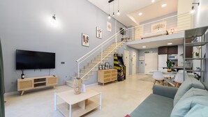 Un vaste salon doté d’un téléviseur à écran plat, d’un escalier menant à un niveau supérieur, d’un coin cuisine et d’un espace détente avec un canapé et des fauteuils.