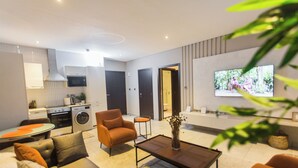 Un salon moderne comprenant un canapé, un fauteuil, une table basse et un téléviseur fixé au mur.