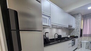A modern kitchen with a stainless steel refrigerator, white cabinets, a microwave, and a gas stove. - ER21C - Bombinhas Center Residential (Bombinhas)