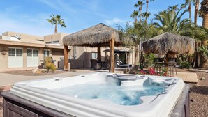 A hot tub in a backyard with a thatched-roof gazebo, palm trees, and a building with a flat roof. - Scottsdale Luxury Villa w/ Pool, Hot Tub, Pickleball, Mini-Golf, Basketball (Scottsdale)