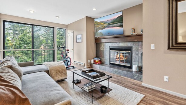 A modern living room with a fireplace, large windows, a sofa, and a bike. - Eagle River Retreat I Hot tub & Pool (Avon)