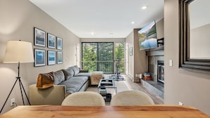 A modern living room with a sofa, a dining table, a lamp, and a fireplace. - Eagle River Retreat I Hot tub & Pool (Avon)
