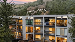 A multi-story building with balconies, large windows, and a view of a forested hillside. - Eagle River Retreat I Hot tub & Pool (Avon)