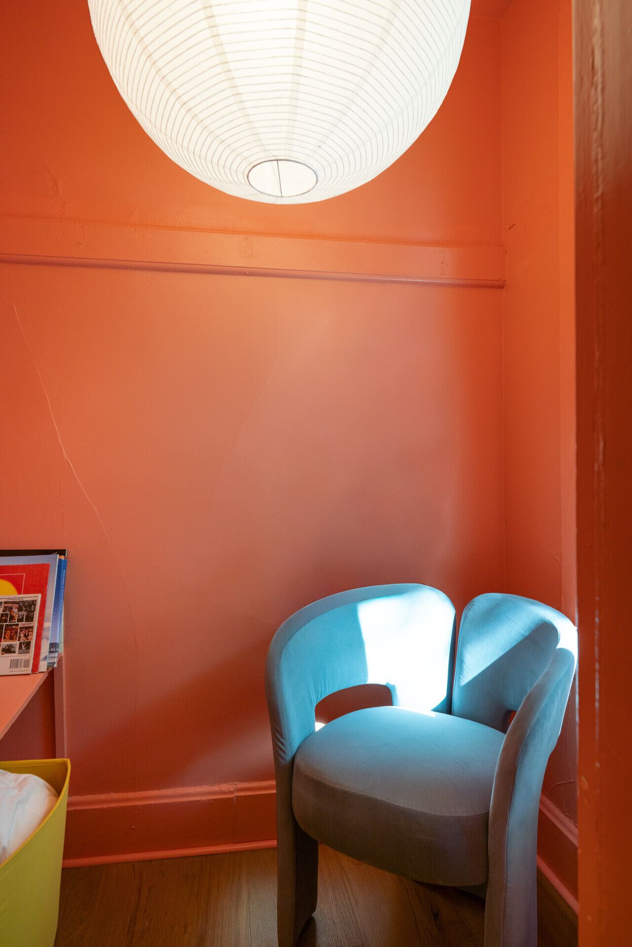 A room with a single blue chair, a bookshelf with books, and a white ceiling light fixture.