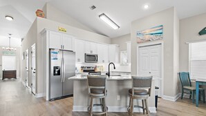 Una cocina moderna con armarios blancos, un refrigerador de acero inoxidable, un microondas y una isla con dos taburetes.