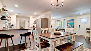 Una cucina moderna con mobili bianchi, un'isola centrale e un'area pranzo con tavolo e sedie in legno.