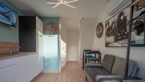 A modern kitchen with a wooden countertop and cabinets, a dining area with a grey sofa and a small table, and a wall with a globe and a clock. - Au Bonheur Du Voyageur - Proche gare routière (Vannes)