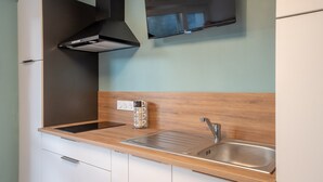 A kitchen with a stainless steel sink, a wooden countertop, a black range hood, and a wall-mounted television. - Au Bonheur Du Voyageur - Proche gare routière (Vannes)