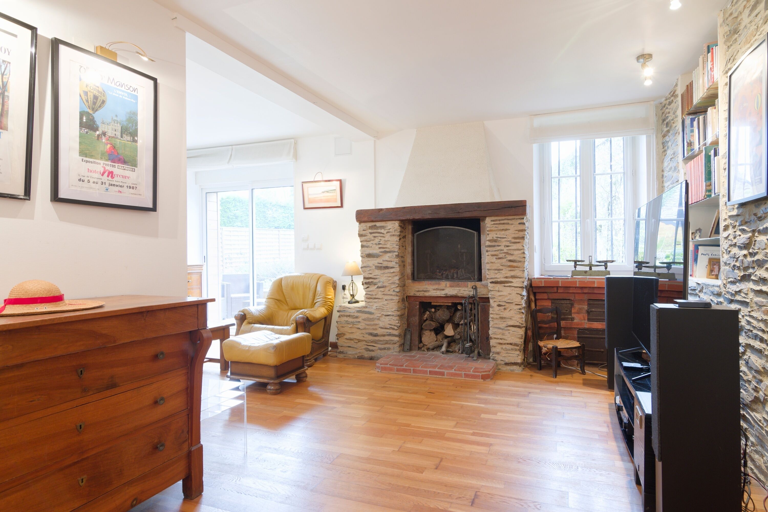 A spacious living room with a stone fireplace, wooden furniture, and a bookshelf.