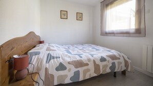 Makuuhuoneessa on puinen sängynpääty, kuviollinen peitto sängyllä, yöpöytälamppu ja kaksi kehystettyä kuvaa seinällä.