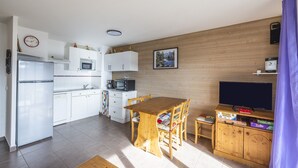 Kompakti keittiö, jossa on valkoiset kaapit, puinen ruokapöytä ja televisio puisen kaapin päällä.