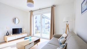 Een moderne woonkamer met een bank, televisie, houten kast en een groot raam met gordijnen.