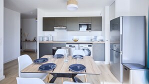 Een moderne keuken met een eethoek, roestvrijstalen apparatuur en een lichte houten tafel.