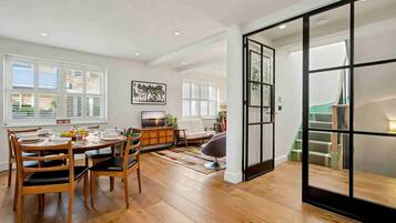 A modern living room with a dining area, wooden flooring, and a staircase leading to an upper level.
