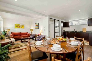 A modern living room with a sofa, chairs, a dining table set for four, and a kitchen in the background. - Ruston Mews – Notting Hill Hideaway (London)