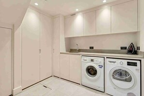 A laundry room with two front-loading washing machines, a built-in ironing station, and a countertop. - Ruston Mews – Notting Hill Hideaway (London)