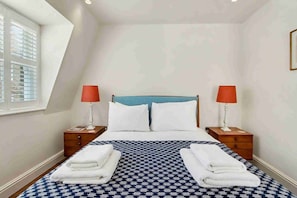 A hotel room with a bed, two bedside tables, a window, and a checkered bedspread. - Ruston Mews – Notting Hill Hideaway (London)