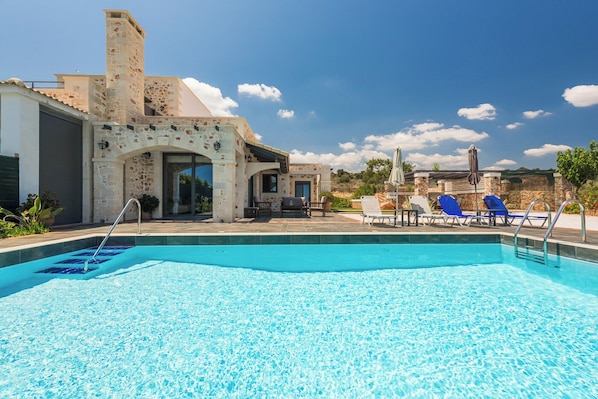 A swimming pool with lounge chairs and a stone building with an arched entrance. - Villa Resi, Vamos, Private Pool, Sea View-5 minutes to the beach! (Chania)