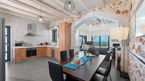 A modern kitchen with stone walls, wooden cabinets, and a dining area with a view. - Villa Resi, Vamos, Private Pool, Sea View-5 minutes to the beach! (Chania)