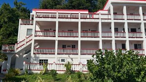 Um edifício com vários andares, varandas, telhado vermelho e fachada branca.