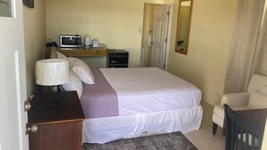 Quarto com cama, mesa de cabeceira, luminária e uma pequena escrivaninha com computador e outros objetos.