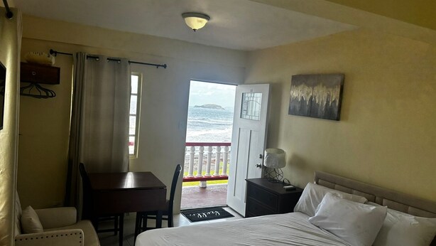 Quarto de hotel com cama, escrivaninha, cadeira, mesa de cabeceira e um quadro na parede.