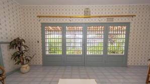 Une pièce avec un papier peint à motifs, une plante en pot, un sol carrelé et un ensemble de portes doubles dotées d’une grille métallique.