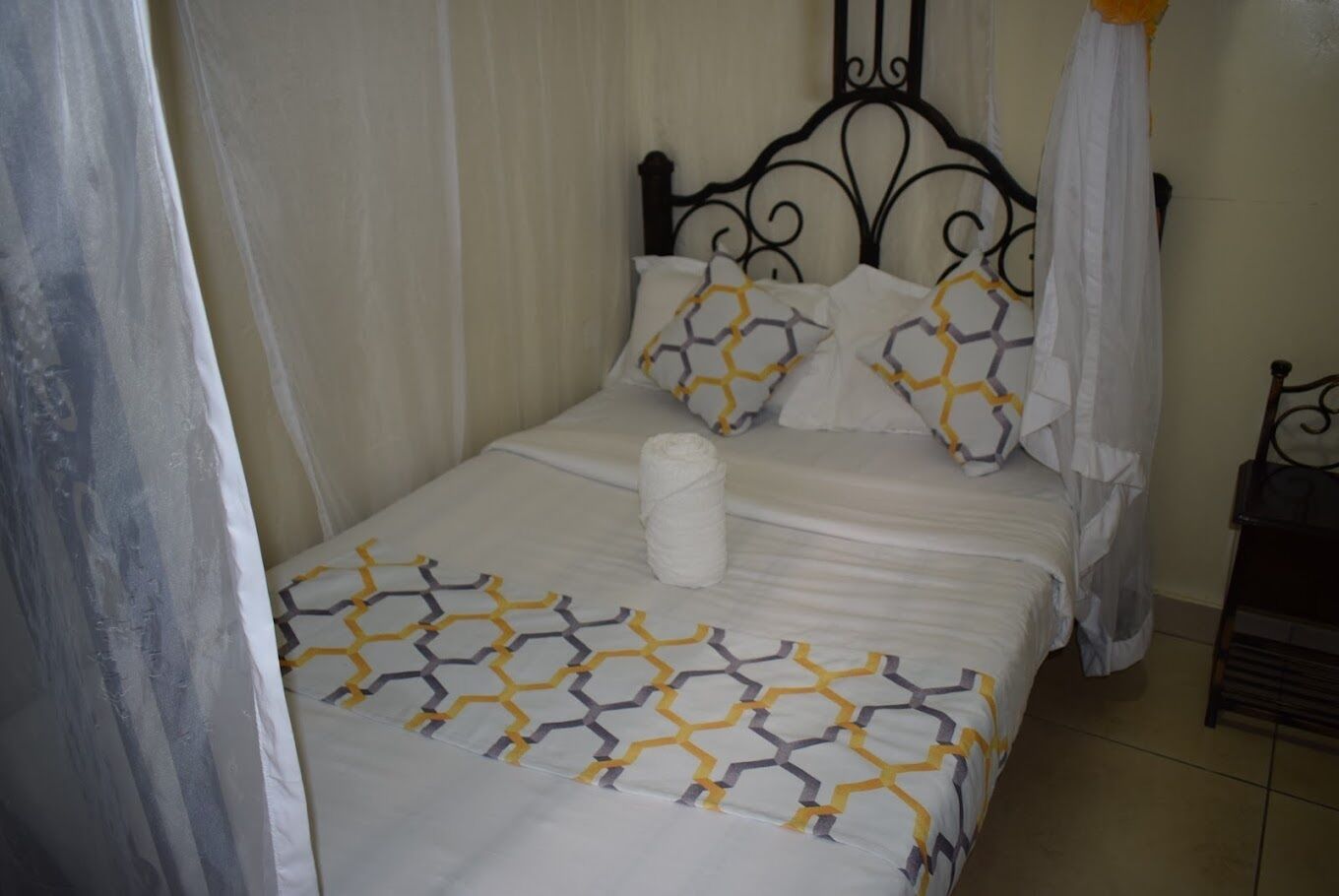 Una cama bien tendida con una colcha de estampado geométrico, una almohada blanca y una toalla blanca enrollada.