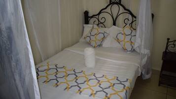 Una cama bien tendida con una colcha de estampado geométrico, una almohada blanca y una toalla blanca enrollada.