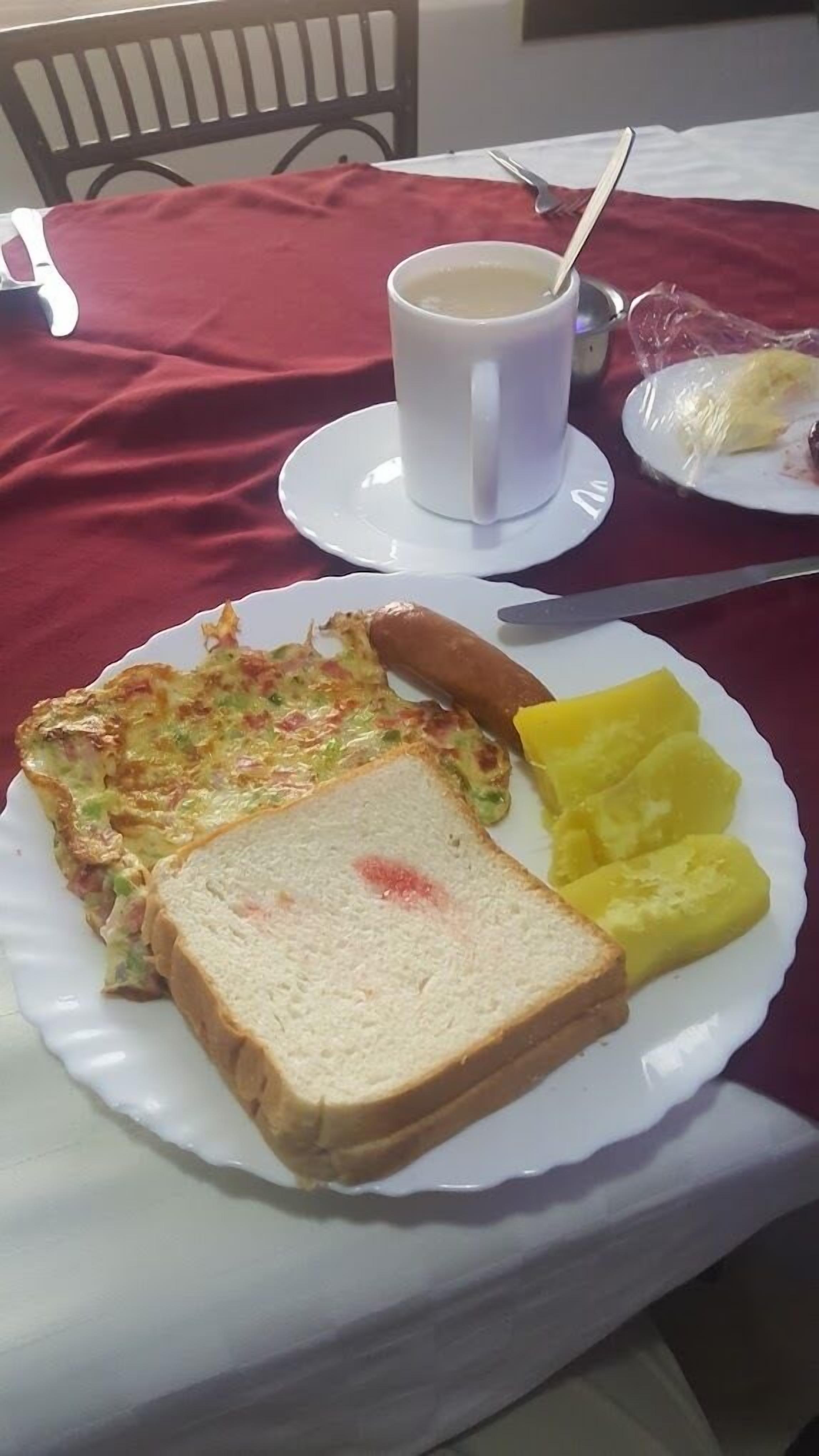 A plate with a sandwich, a hot dog, and yellow fruit on a table with a red tablecloth.