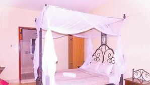 A four-poster bed with a canopy, a wooden nightstand, and a door leading to a bathroom. - Northern Galaxy Hotel Isiolo (Isiolo)
