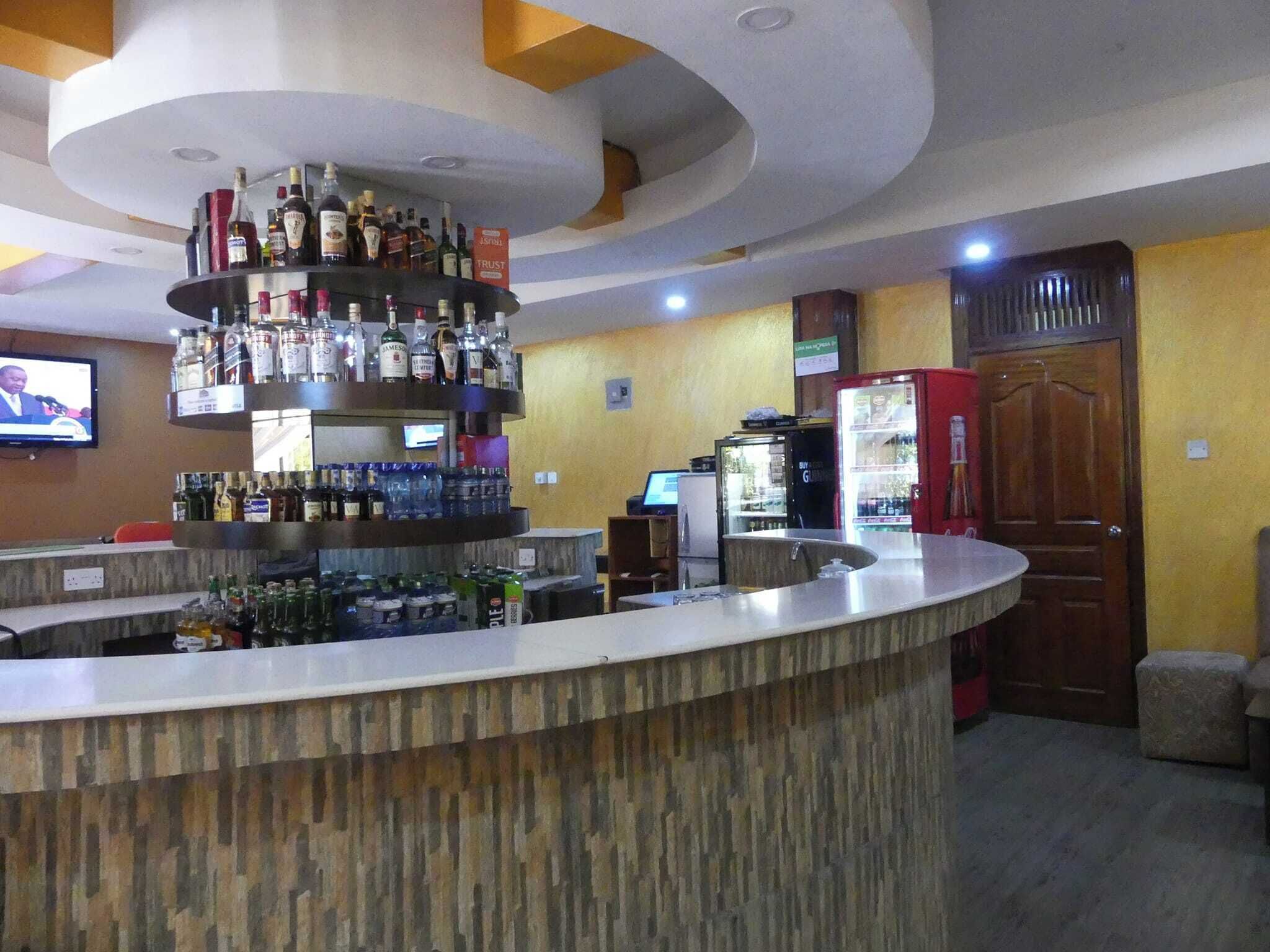 Zona de bar con un mostrador central para licores, una pantalla de televisión y un refrigerador.
