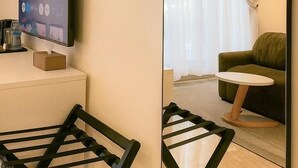 A hotel room with a large mirror reflecting a living area, a television on a stand, and a small table with a chair. - Mayhill Signature (Lekki)