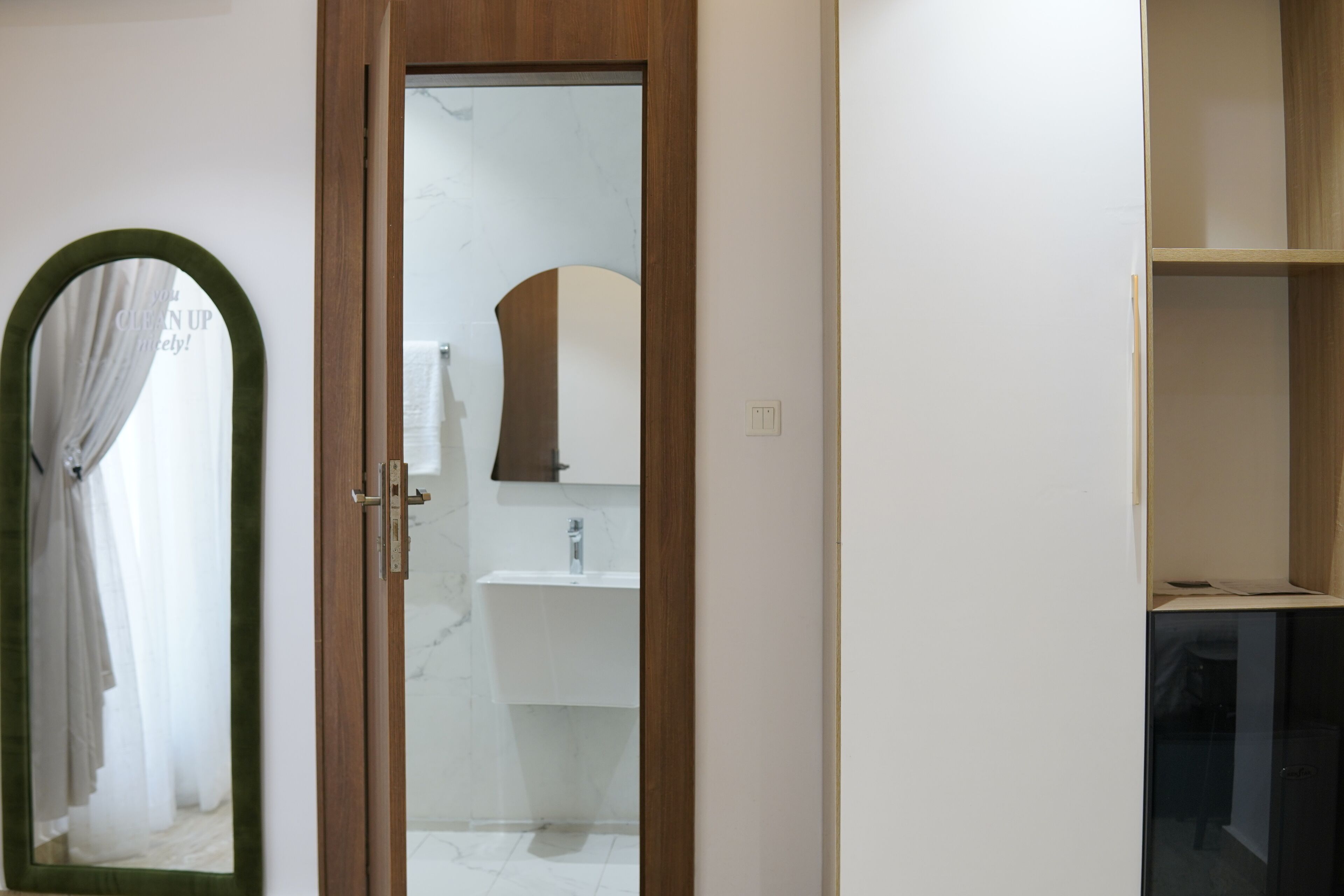 Ein Badezimmer mit Holztür, Spiegel, Waschbecken und Duschbereich.