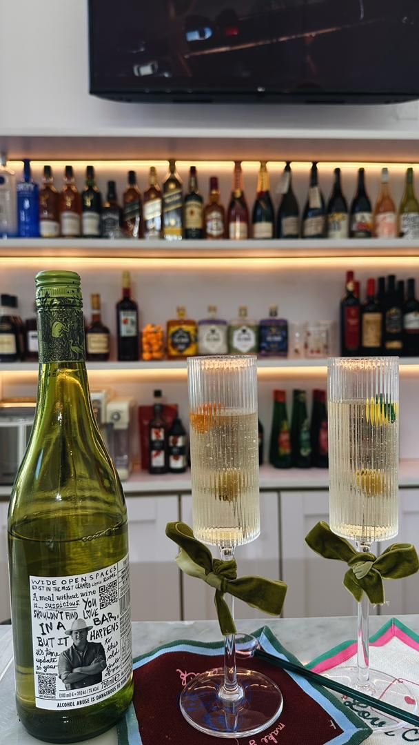 A bottle of wine and two glasses with a decorative ribbon, placed on a table with a colorful placemat.