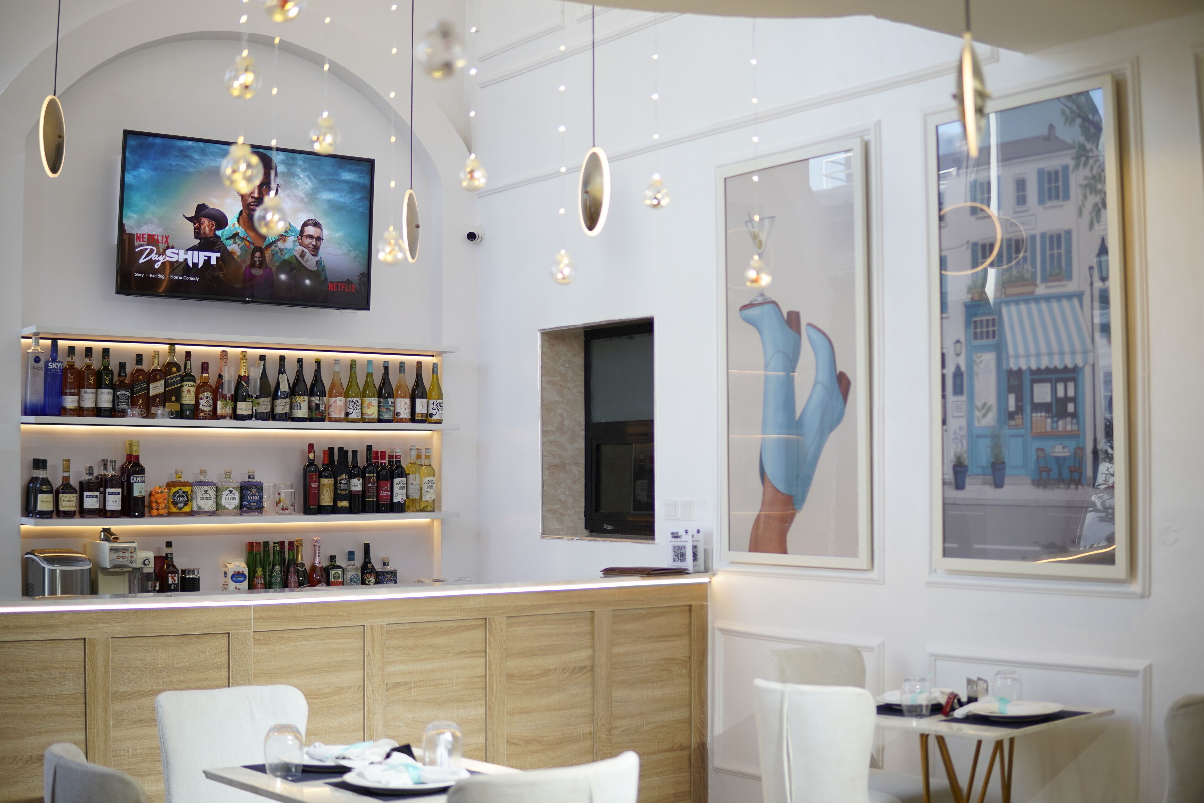 A bar area with a television displaying a Netflix show, shelves of liquor, and a large window with a city view.