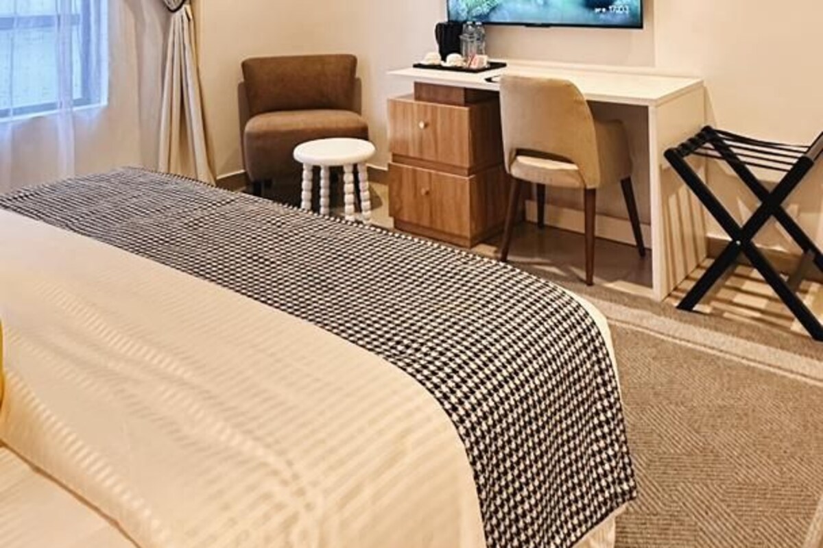 A hotel room with a bed, a desk, a chair, a TV, and a window with curtains.