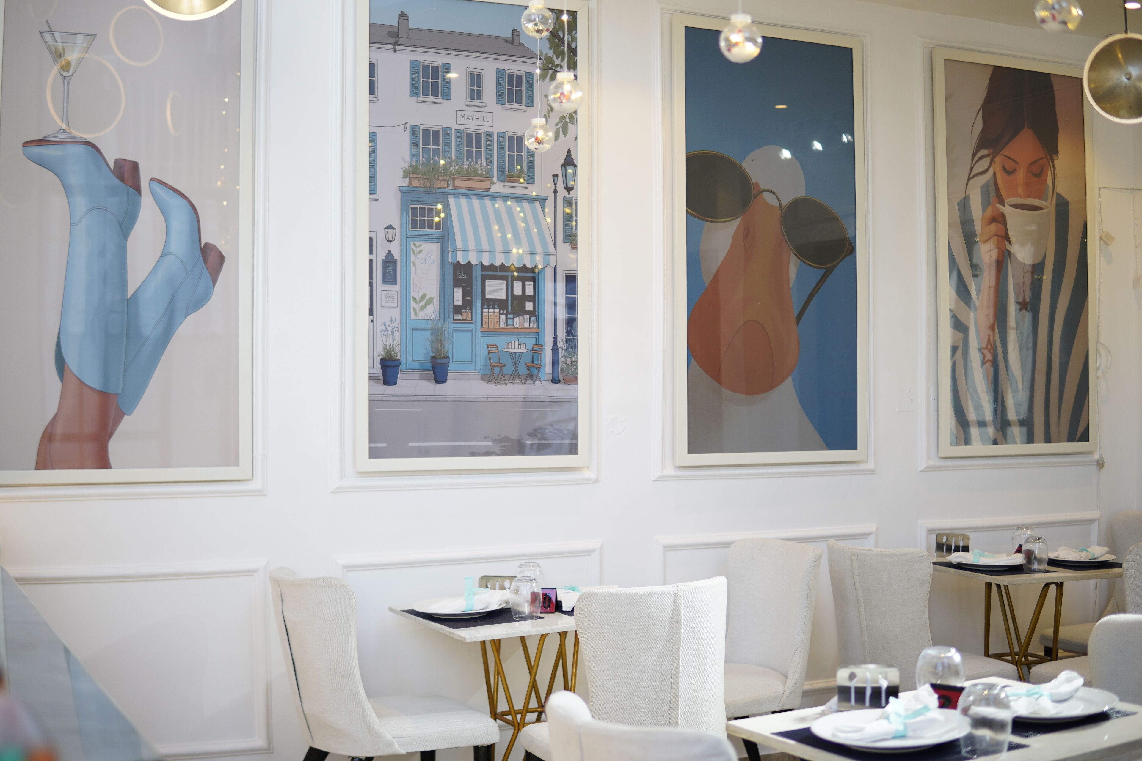 L’intérieur d’un restaurant avec des murs blancs, des œuvres d’art encadrées et une table mise pour le repas.