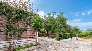 Un patio con suelo de baldosas, una pérgola cubierta de plantas trepadoras, un área de descanso con bancos y una pared con diseño geométrico.