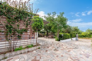 Ein Innenhof mit gefliestem Boden, einer mit Kletterpflanzen bewachsenen Pergola, einer Sitzgelegenheit mit Bänken und einer Wand mit geometrischem Muster.