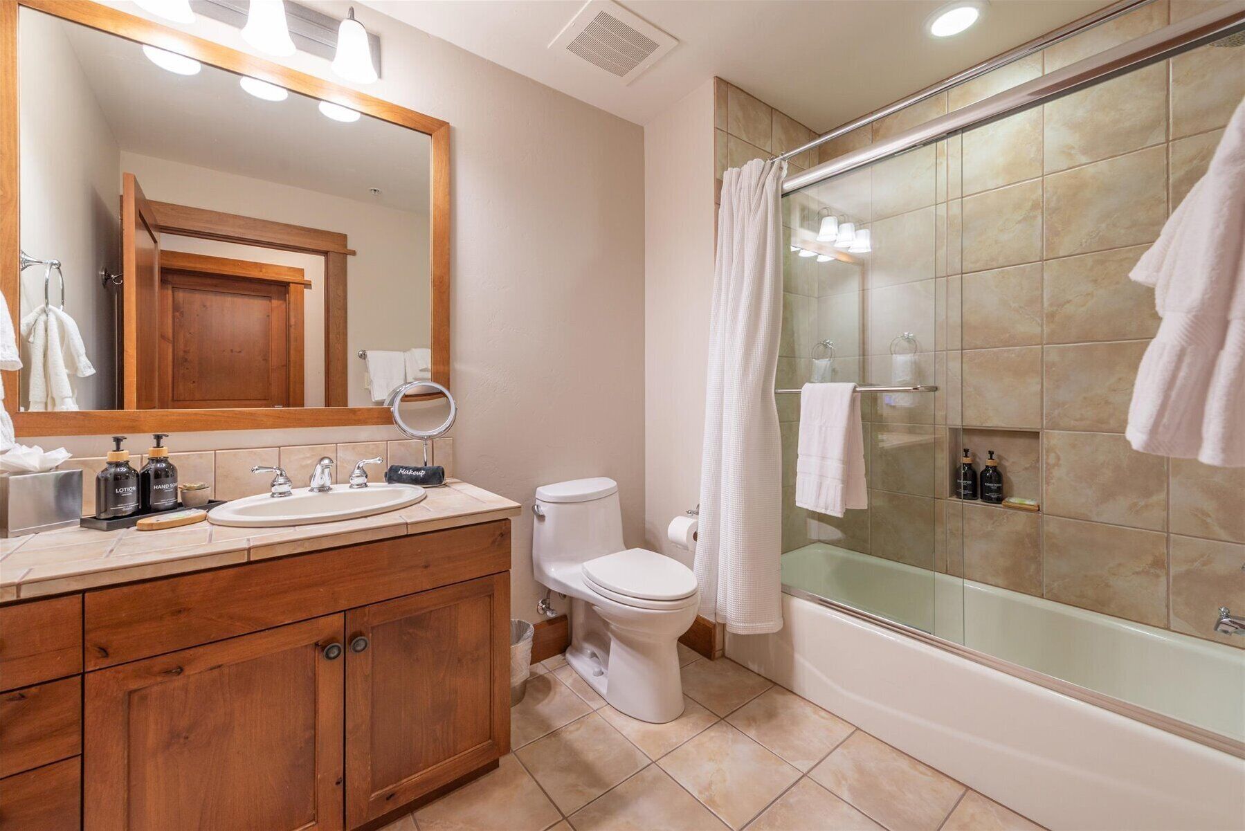 A bathroom with a wooden vanity, two sinks, a toilet, and a glass-enclosed shower area.