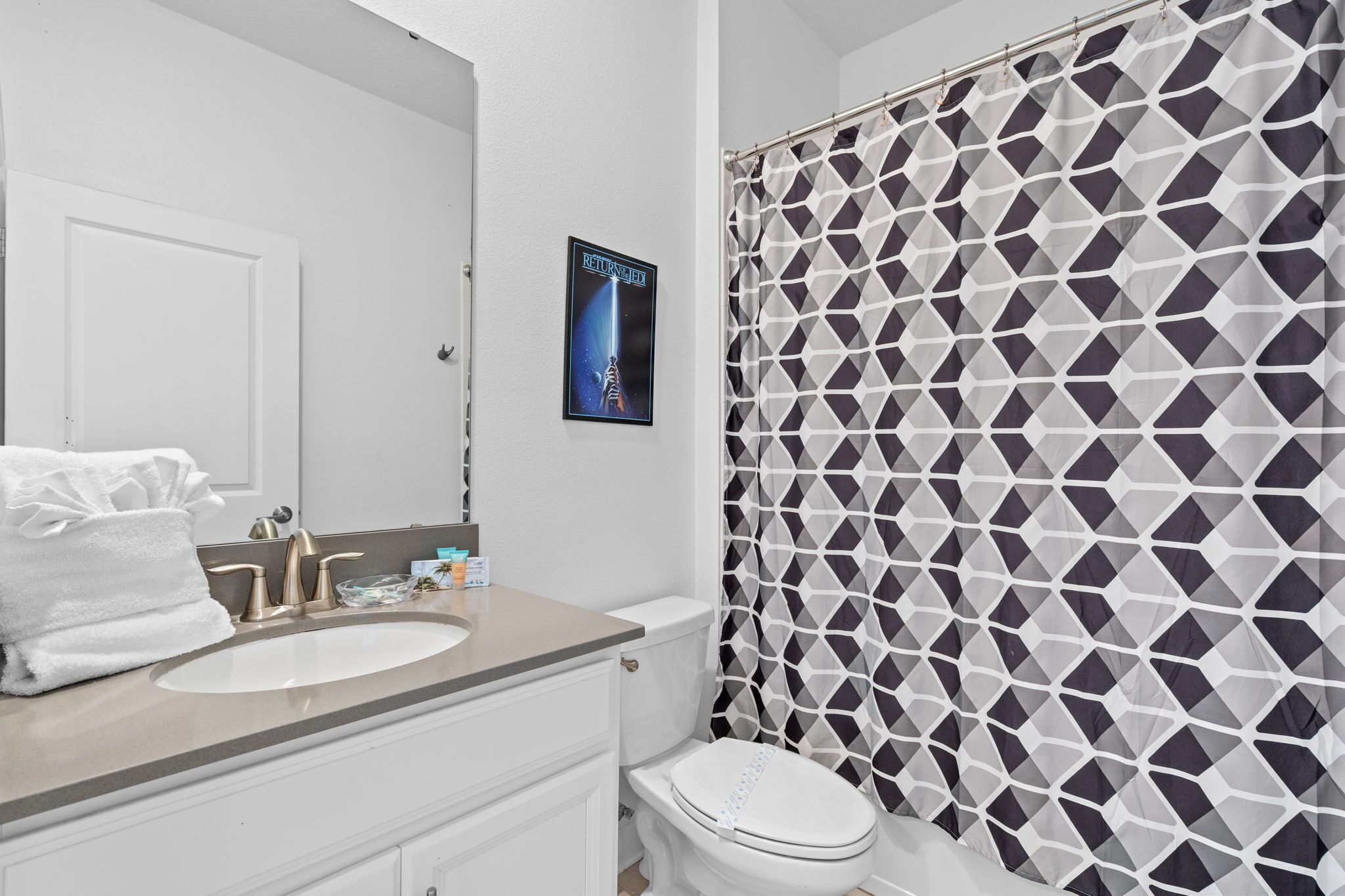 A bathroom with a white sink, a mirror, a toilet, and a shower curtain with a geometric pattern.