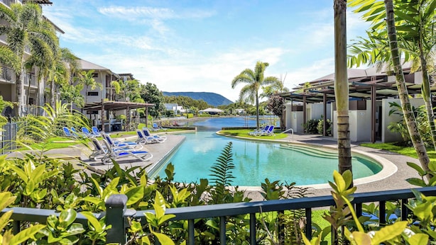 A resort pool with lounge chairs, surrounded by palm trees and greenery, with buildings in the background. - Laguna Escape—Swim-Out Retreat near Sea & Dining (Trinity Beach)