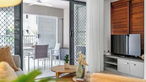 A modern living room with a TV, a dining area, and a balcony with a view. - Laguna Escape—Swim-Out Retreat near Sea & Dining (Trinity Beach)